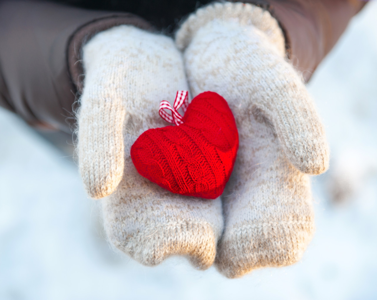 Yün ipten örülmüş küçük bir kalp tutan eldivenli eller