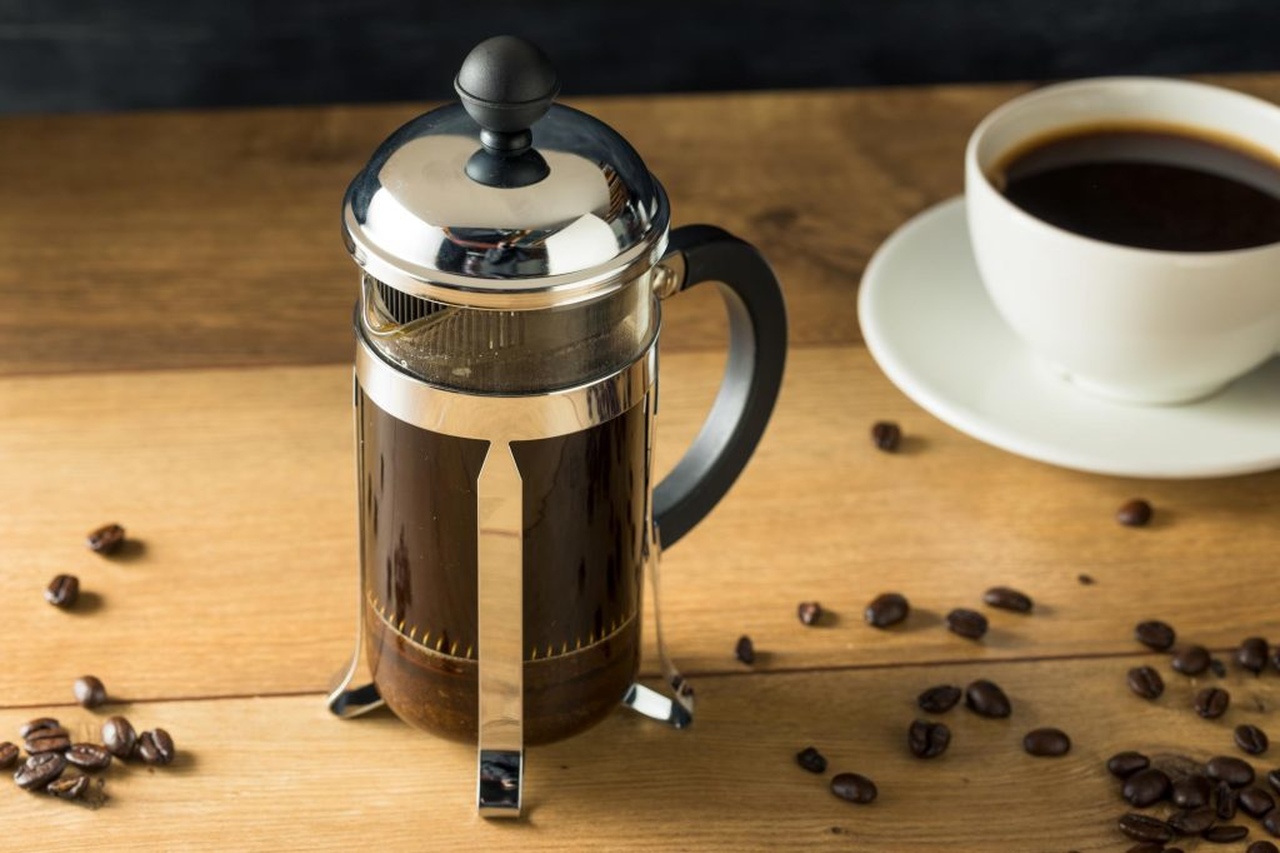 Kahve dolu french press ve yanında duran beyaz kahve fincanı