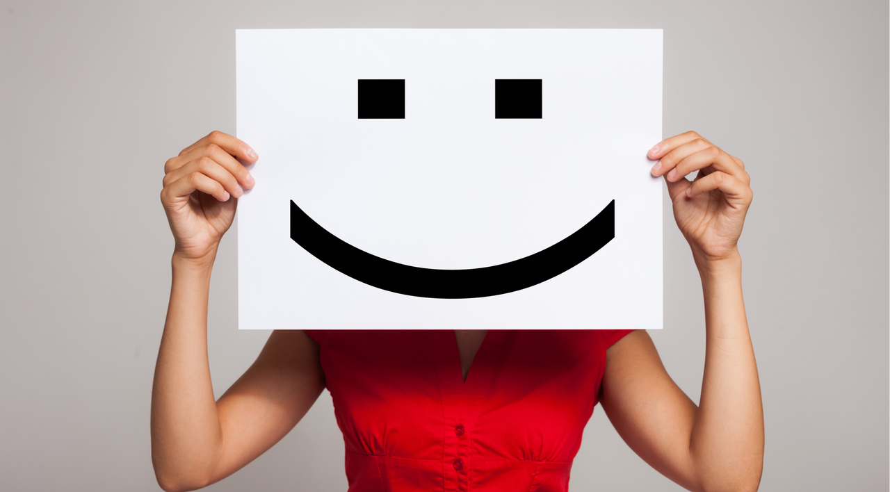 ellerinde yüz hizasına gelecek şekilde gülen suratlı karton tutan kırmızı elbiseli kadın