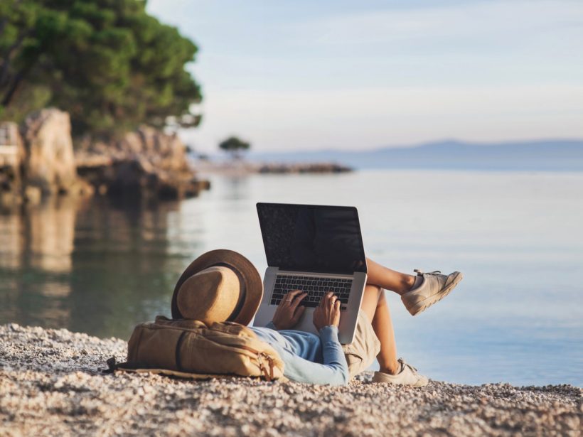 Freelance nedir sorusuna yanıt niteliğinde deniz kıyısında güneşlenirken bilgisayarı ile çalışan kadın