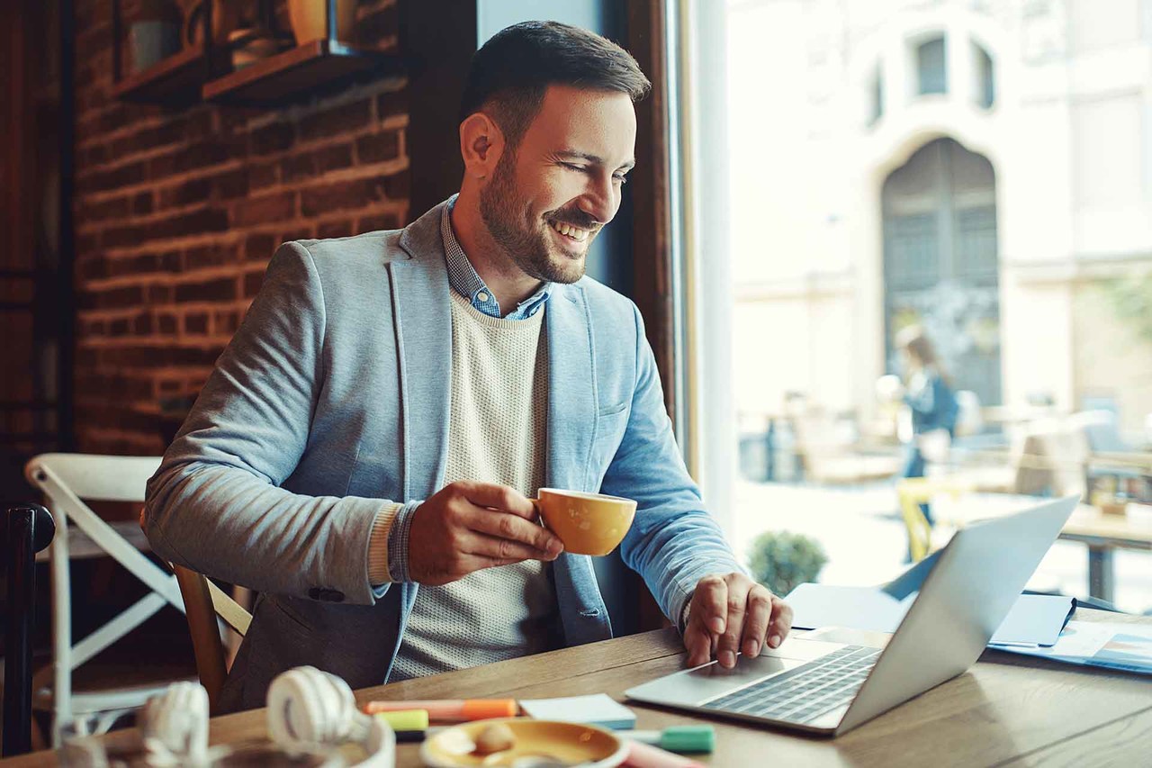 Kahvesini içerken bilgisayarı ile freelance çalışan mutlu adam