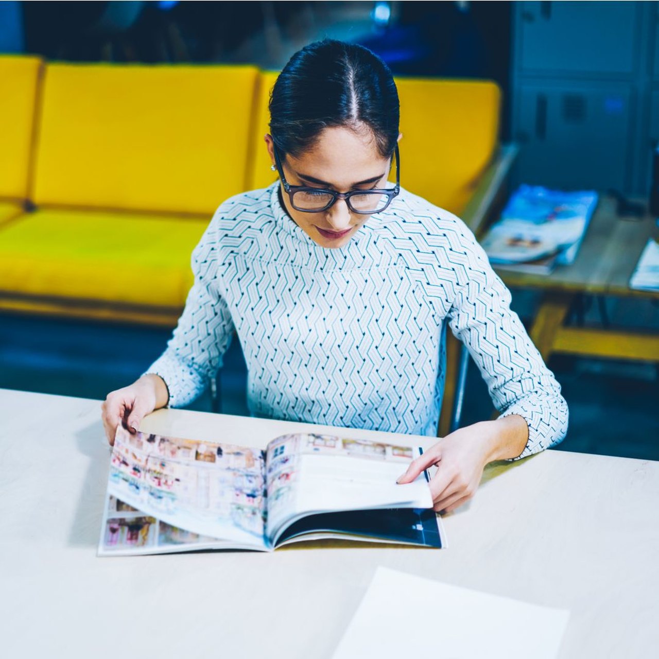 Masaya koyduğu kataloğu inceleyen gözlüklü kadın