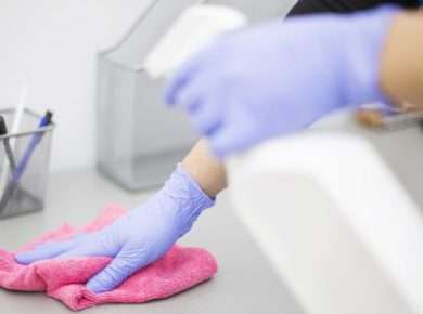 Pembe bir bez ve dezenfektan ile iş yerini temizleyen eldivenli bir kişi