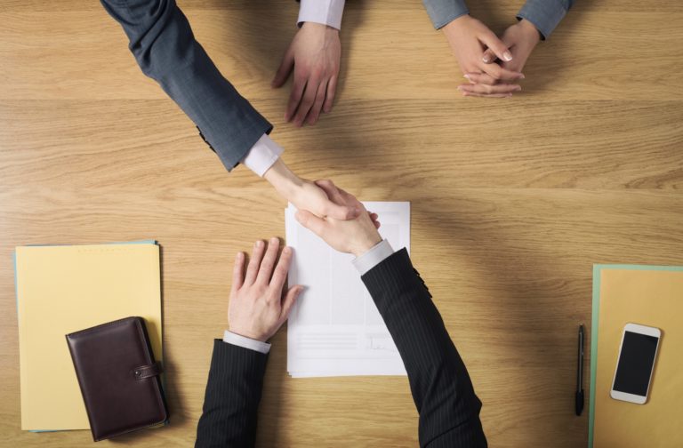 anlaşma sonrası el sıkışan iki erkeğin ve masanın üstten görünümü